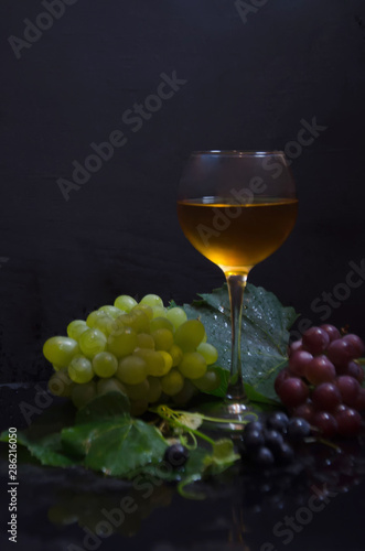 grape brush and leaves and wine glass on black background selective focus