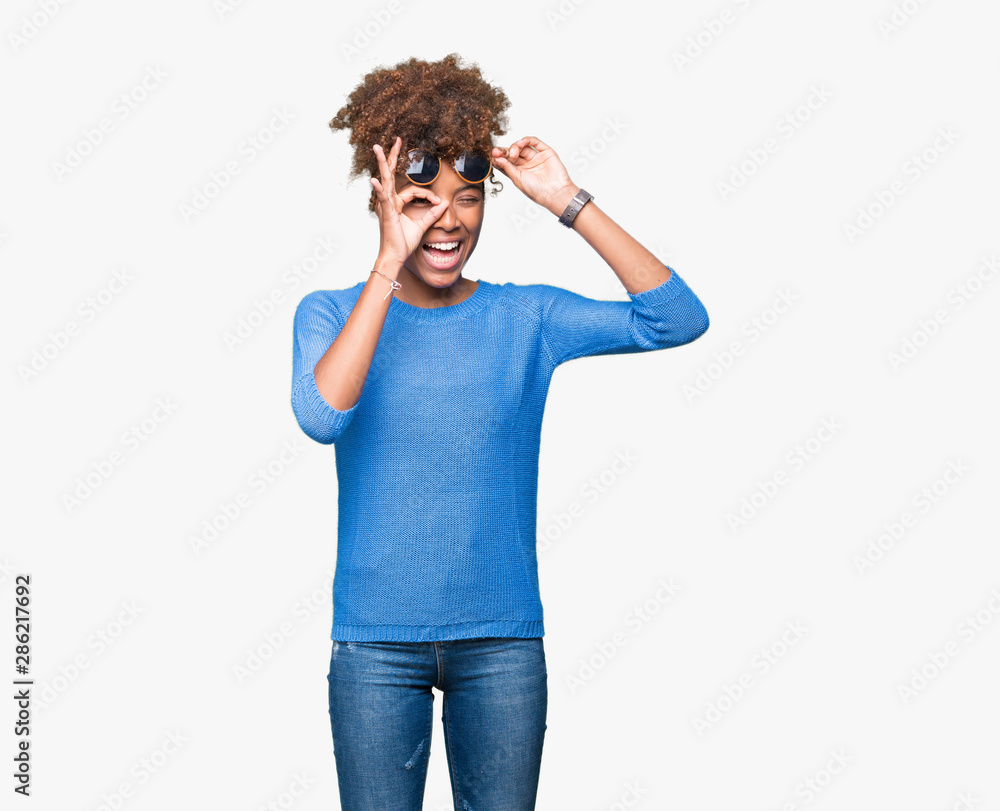 Beautiful young african american woman wearing sunglasses over isolated background doing ok gesture with hand smiling, eye looking through fingers with happy face. Beautiful young african american woman wearing sunglasses over isolated background doing ok gesture with hand smiling, eye looking through fingers with happy face.