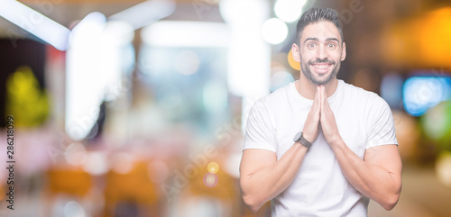 Young man wearing casual white t-shirt over isolated background praying with hands together asking for forgiveness smiling confident.