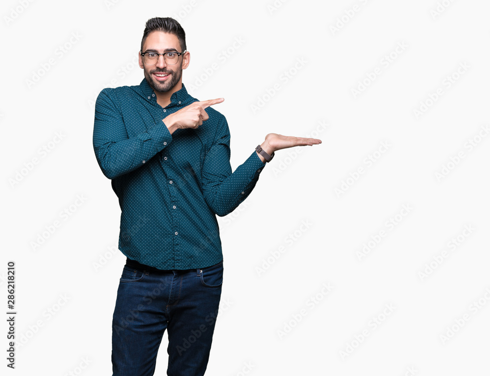 Young handsome business man wearing glasses over isolated background amazed and smiling to the camera while presenting with hand and pointing with finger. Young handsome business man wearing glasses over isolated background amazed and smiling to the camera while presenting with hand and pointing with finger.