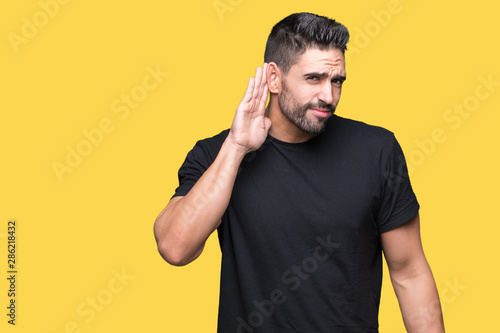 Young handsome man over isolated background smiling with hand over ear listening an hearing to rumor or gossip. Deafness concept. © Krakenimages.com