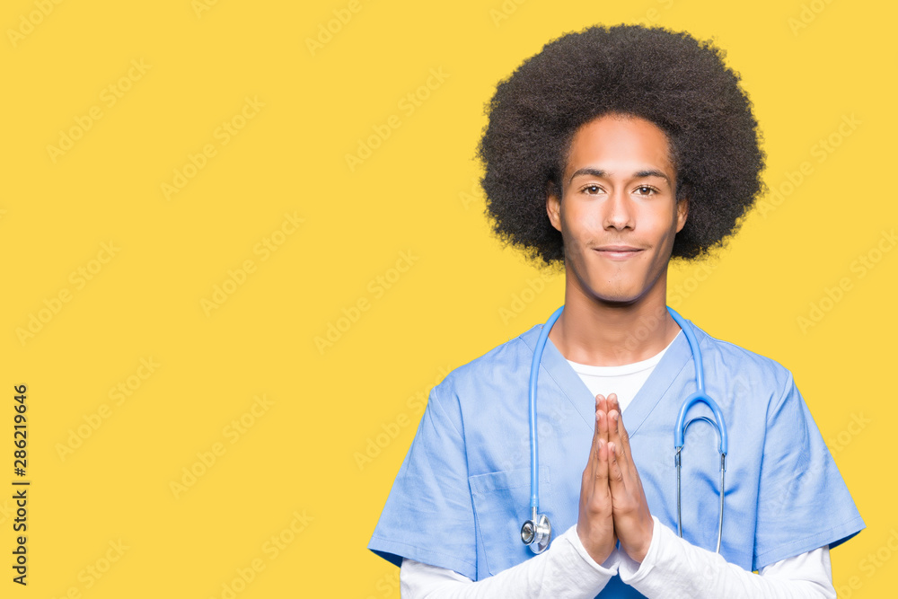 Young african american doctor man with afro hair praying with hands together asking for forgiveness smiling confident. Young african american doctor man with afro hair praying with hands together asking for forgiveness smiling confident.