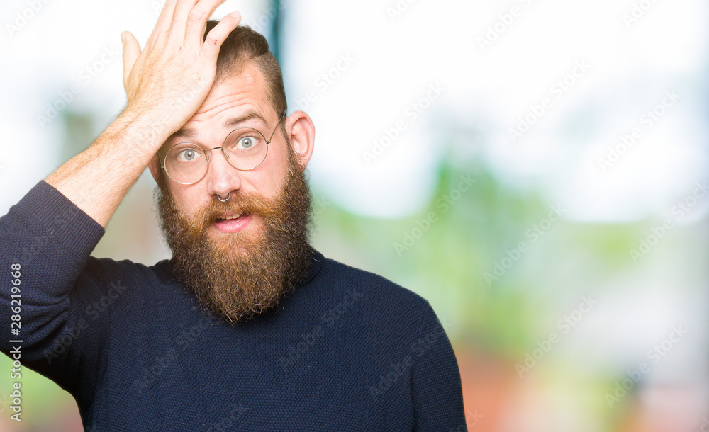 Obraz premium Young blond man wearing glasses and turtleneck sweater surprised with hand on head for mistake, remember error. Forgot, bad memory concept.