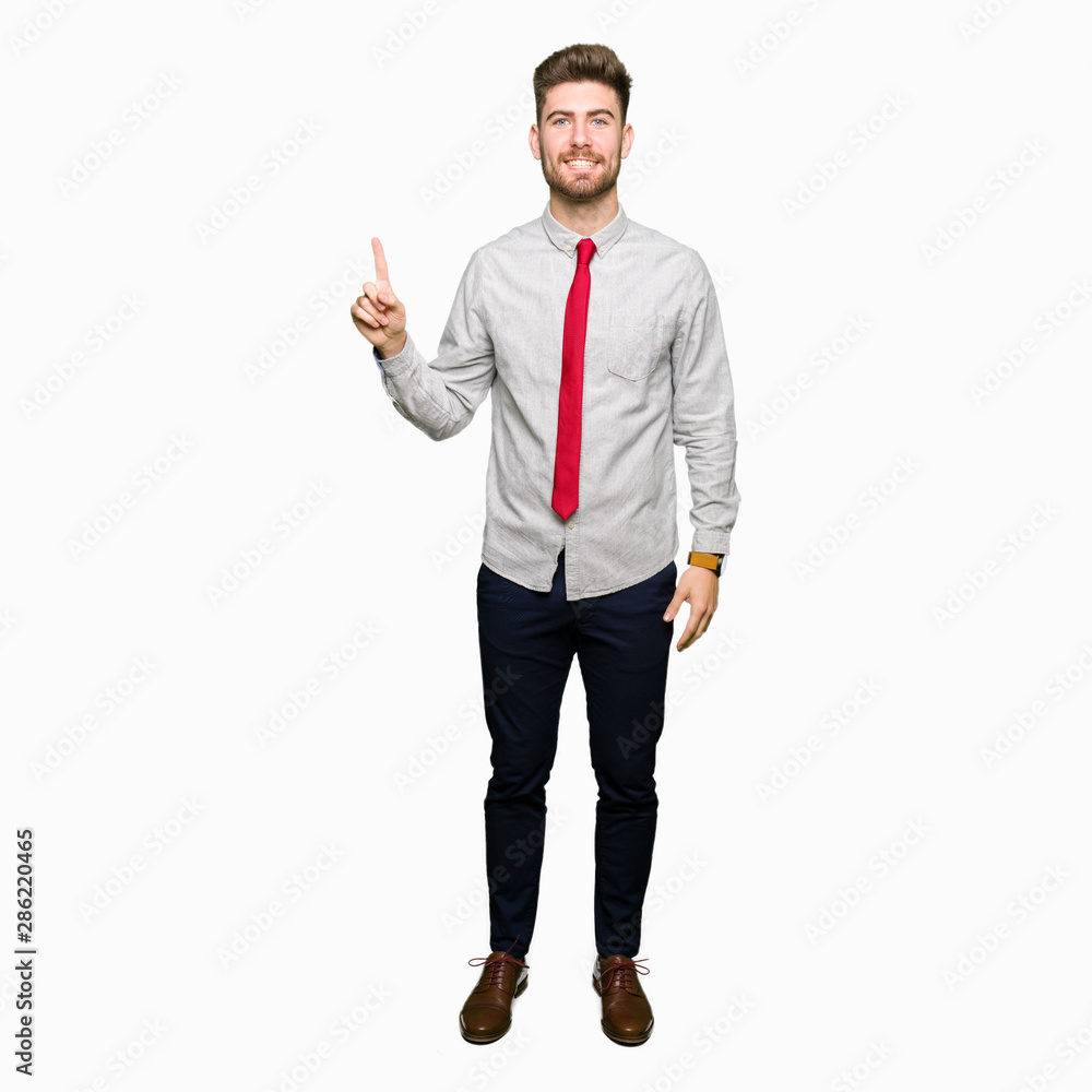 Young handsome business man showing and pointing up with finger number one while smiling confident and happy.