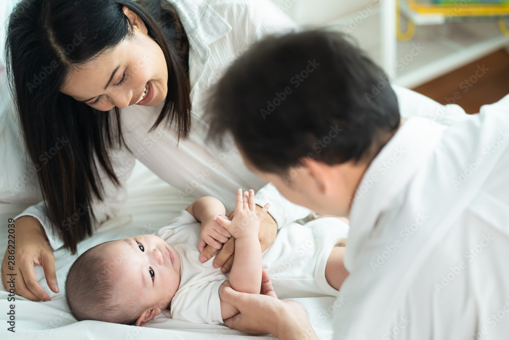 Asian father and mother are playing with new newborn baby on sofa. They are smiling and warm touching to the baby with love. Parents holding both of baby hand. Happy family concept. Asian father and mother are playing with new newborn baby on sofa. They are smiling and warm touching to the baby with love. Parents holding both of baby hand. Happy family concept.