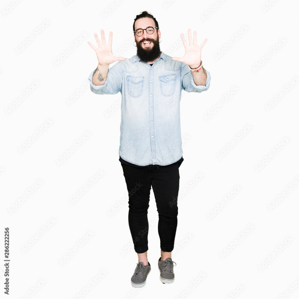 Young hipster man with long hair and beard wearing glasses showing and pointing up with fingers number ten while smiling confident and happy.