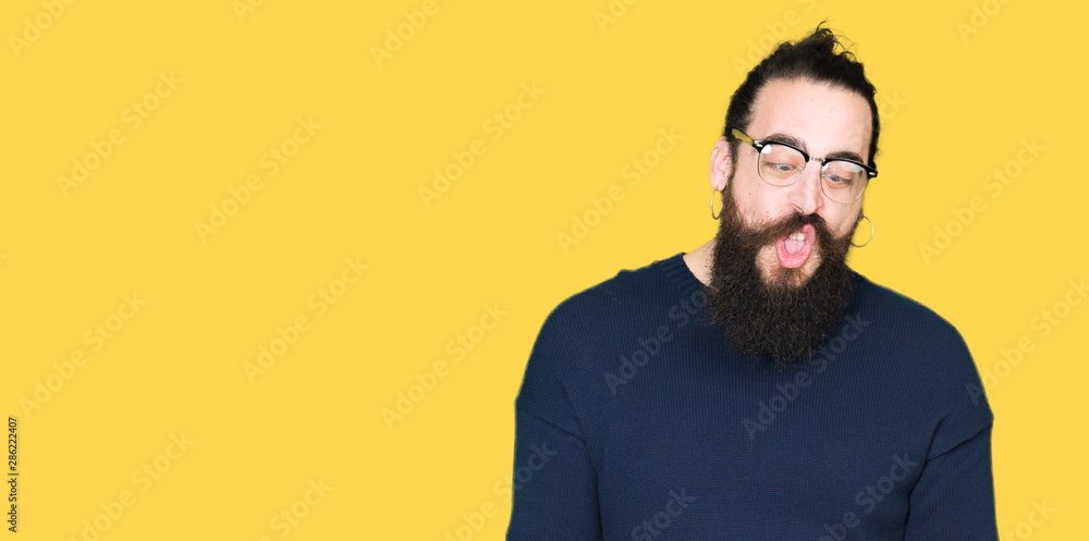 Young hipster man with long hair and beard wearing glasses making fish face with lips, crazy and comical gesture. Funny expression. Young hipster man with long hair and beard wearing glasses making fish face with lips, crazy and comical gesture. Funny expression.