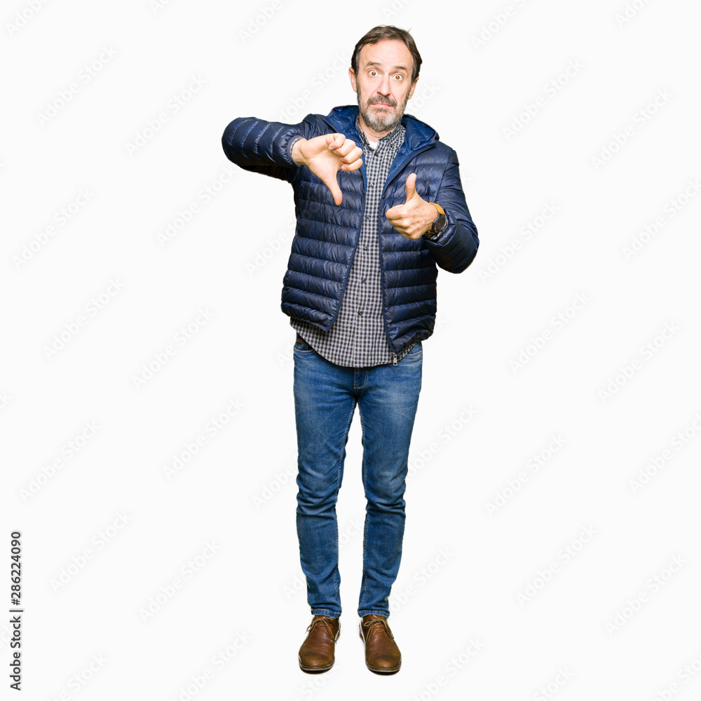 Middle age handsome man wearing winter coat Doing thumbs up and down, disagreement and agreement expression. Crazy conflict Middle age handsome man wearing winter coat Doing thumbs up and down, disagreement and agreement expression. Crazy conflict