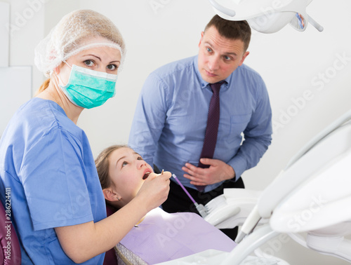 Female stomatologist treating girl with worried father