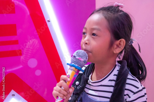 Children holding a microphone singing in the room with neon lights.