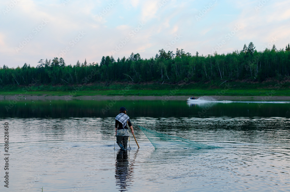 Two men-Yakuts and graceful girl in a Shawl in the background of a boat go in wading boots through the wild North river Vilyui, which are traditionally caught by the dragnet of the local fish tugun.