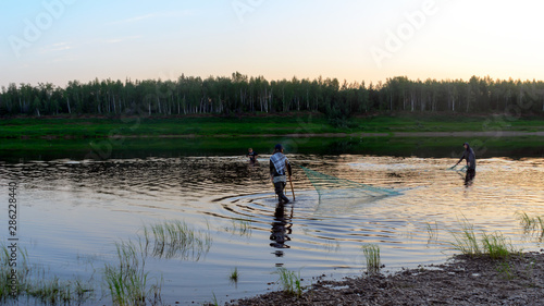 Принти на полотні Two men Yakuts and graceful girl in a shawl to go wading boots dragnet for wildlife in the river Vilyuy in a forest traditionally catching local fish tugunok
