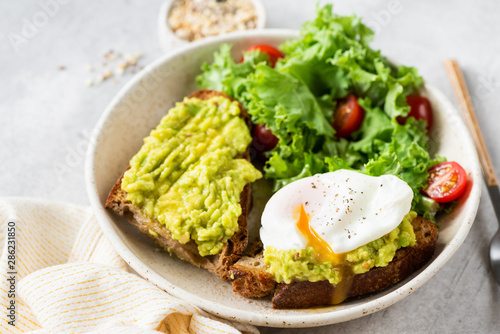 Delicious rye bread toast with avocado and poached egg served with kale and tomato salad. Healthy vegetarian food, clean eating and dieting concept