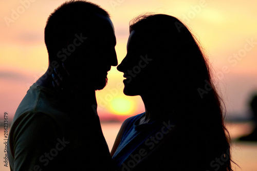 Silhouettes of a guy and a girl on a sunset background. Hugs of a couple in love. Lovers man and woman in each other's arms. Couple in love. Love relationship. Couple on a sunset background.