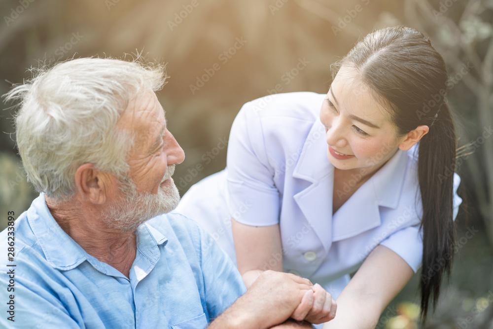 Caring nurse with senior man sitting on wheelchair in gaden. Asian woman, caucasian man. Discussing. With light leaks.