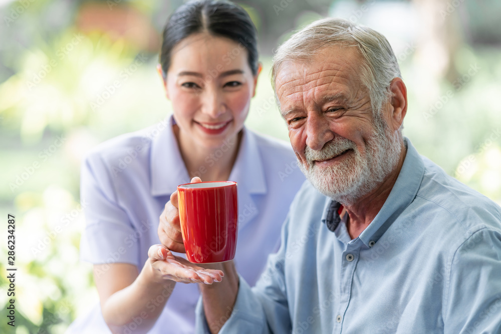 Senior man having breakfast with beautiful nurse in retirement home. Caucasian man with asian woman. Enjoying coffee with nurse. Senior man having breakfast with beautiful nurse in retirement home. Caucasian man with asian woman. Enjoying coffee with nurse.