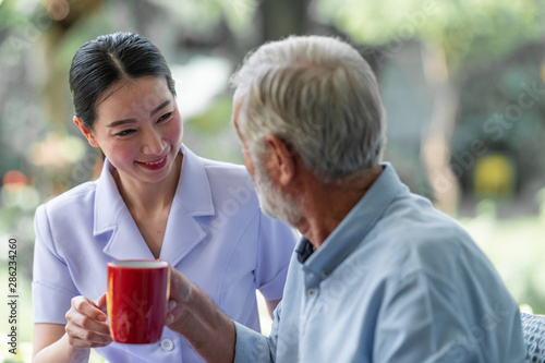 Senior man having breakfast with beautiful nurse in retirement home. Caucasian man with asian woman. Enjoying coffee.