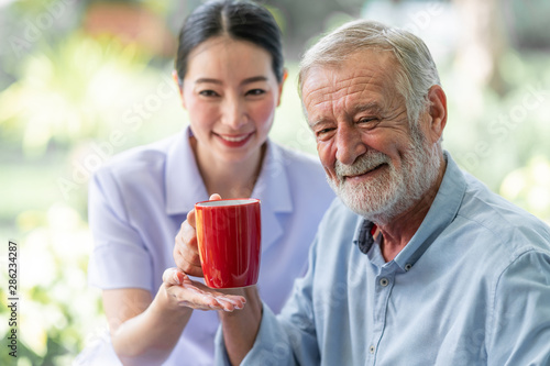 Senior man having breakfast with beautiful nurse in retirement home. Caucasian man with asian woman. Enjoying coffee with nurse.