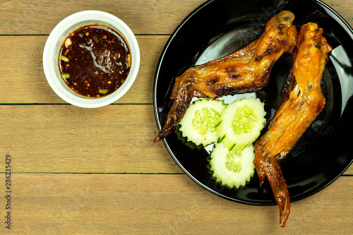 Yummy grilled chicken wings with cucumbers on black dish with wooden table background.