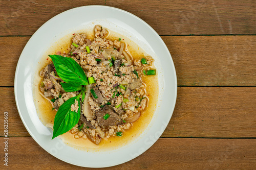 Delicious spicy minced pork and liver salad decoration with basil leaves in white dish on wooden table background.