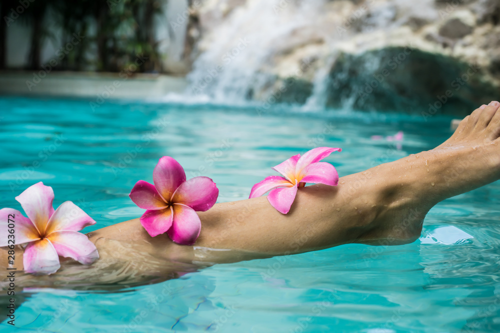 Woman Legs Beauty, Female Smooth Body, Foot Care, Hair Care. Beauty concept of woman legs, female smooth body, female foot in a pool with frangipani colors. Spa concept Woman Legs Beauty, Female Smooth Body, Foot Care, Hair Care. Beauty concept of woman legs, female smooth body, female foot in a pool with frangipani colors. Spa concept