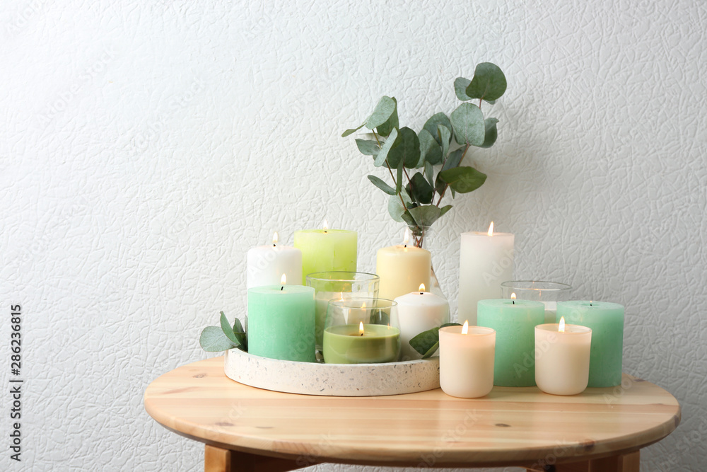 Composition with burning candles on table near white wall Composition with burning candles on table near white wall