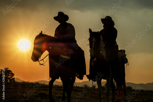 Silhouette of cowboys on horseback at sunset, sports and country lifestyle photo