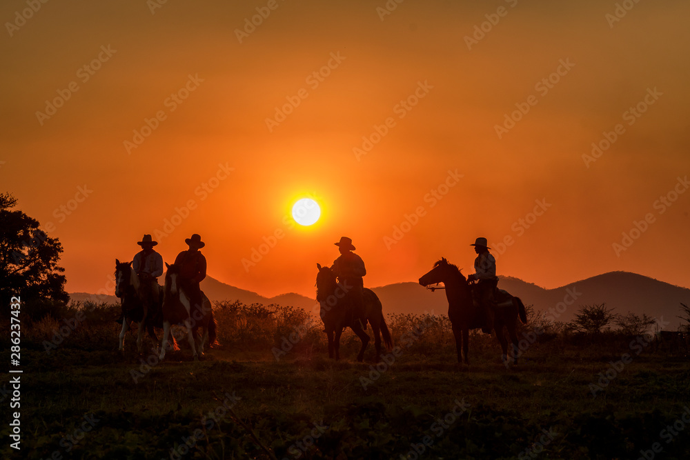 silhouette of cowboys on horseback at sunset with mountain background