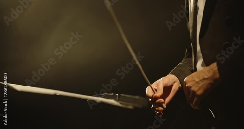 Close up shot of hands of symphony orchesra conductor directing music by waving his baton. Studio shot on black background 4k footage photo
