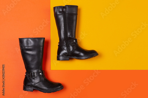 a pair of black leather boots lies on an orange and yellow background, the concept of fashion