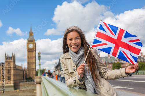 London Big Ben Westminster travel tourist woman showing United Kingdom UK flag. Europe vacation destination Asian girl holding Great Britain british flag Union Jack sign.
