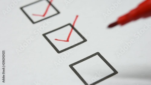 red pen make a check mark sign in check box list on white paper. closed up and selective focus