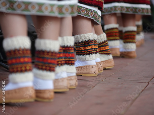 females legs in traditional regional leather folk shoes, woolen socks and lower parts of skirts decorated with traditional Ukrainian pattern