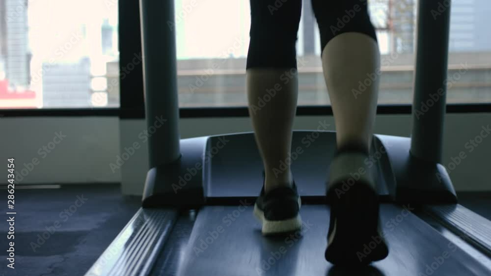Legs of a woman running on a treadmill in a fitness club with a city in the background - close up view - sport concept Legs of a woman running on a treadmill in a fitness club with a city in the background - close up view - sport concept