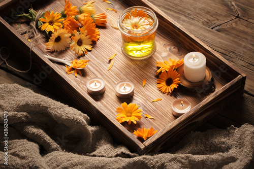 Medicinal flowers of calendula with burning candles on dark woo