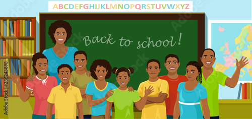 Teacher and pupils are in the schoolroom. African American teacher and children stand in front of the blackboard, bookcase and map. Back to school concept. Vector illustration.