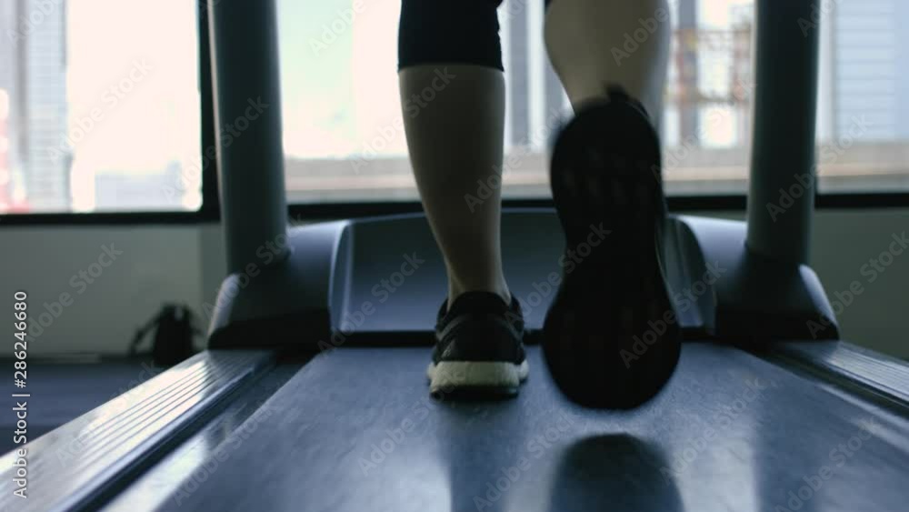 Legs of a woman walking on a treadmill in a fitness club with a city in the background - close up view - sport concept Legs of a woman walking on a treadmill in a fitness club with a city in the background - close up view - sport concept