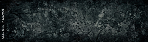 Wide weathered cracked black concrete wall. Black broken cement surface texture. Dark gloomy grunge background