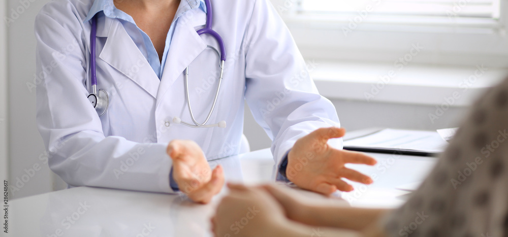 Doctor and patient discussing something while sitting at the desk at hospital, close-up. Medicine and health care Doctor and patient discussing something while sitting at the desk at hospital, close-up. Medicine and health care