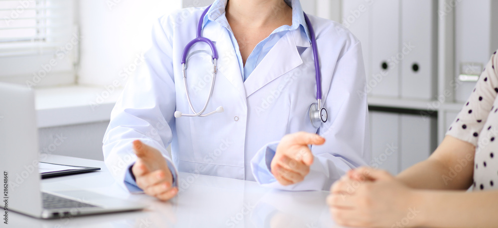 Doctor and patient discussing something while sitting at the desk at hospital, close-up. Medicine and health care Doctor and patient discussing something while sitting at the desk at hospital, close-up. Medicine and health care