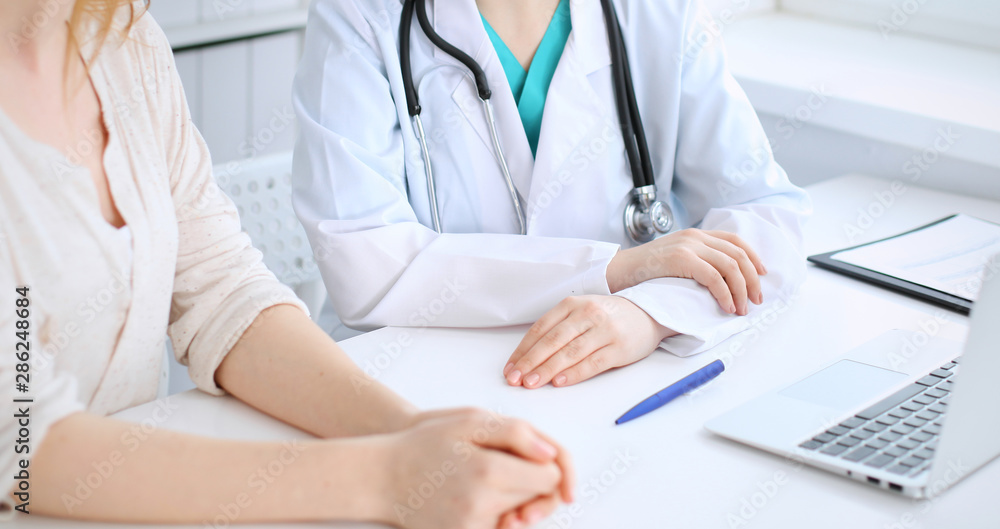 Doctor and patient discussing something while sitting at the desk at hospital, close-up. Medicine and health care Doctor and patient discussing something while sitting at the desk at hospital, close-up. Medicine and health care