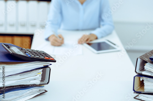 Calculator and binders with papers are waiting to be processed by business woman or bookkeeper back in blur. Internal Audit and tax concept