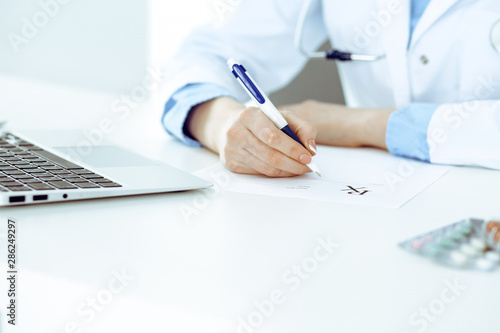 Female doctor filling up prescription form while sitting at the desk in hospital closeup. Healthcare  insurance and excellent service in medicine concept