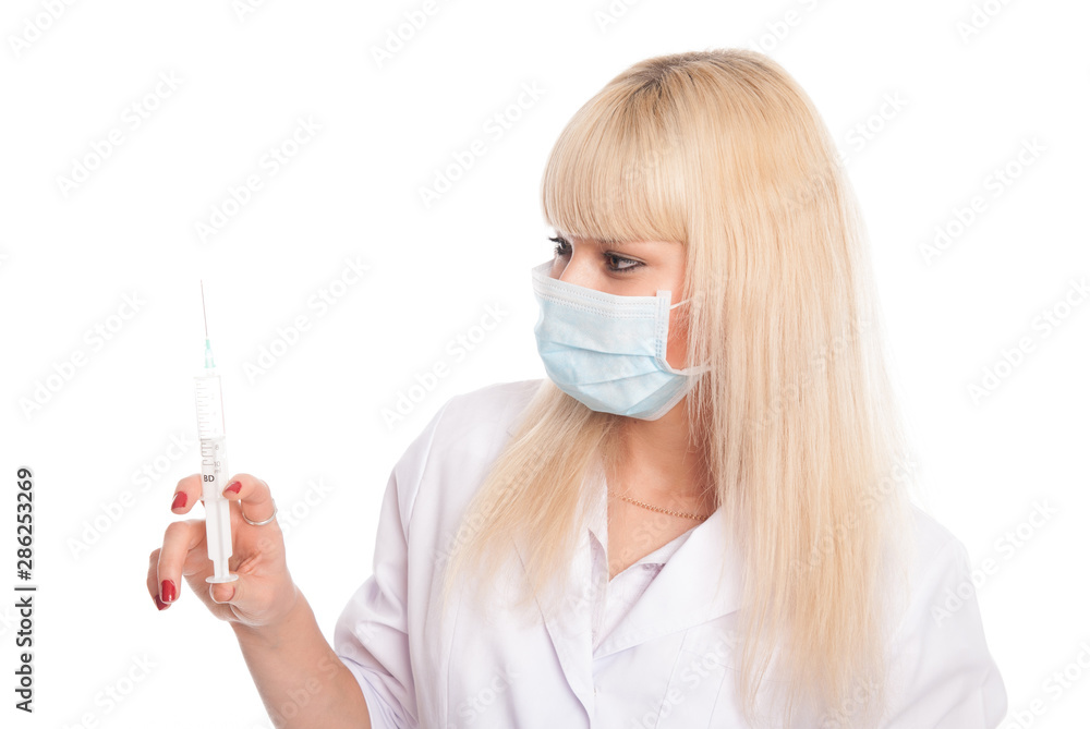 Close-up of a young blonde nurse in a mask looking at a syringe.