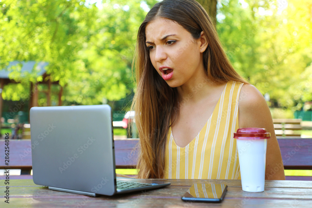 Disappointed business woman sitting in the park looks at the laptop raging after working hard all the morning. Disappointed business woman sitting in the park looks at the laptop raging after working hard all the morning.