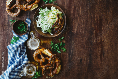 Traditional german appetizer and beer glasses on dark brown wooden table. Mashed potatoes, salad, pretzels and sausages. Oktoberfest party background