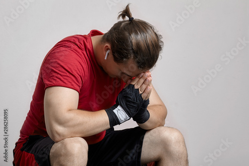 Fotografija Young caucasian man in sport wear and boxing bandages sits with hands to forehead