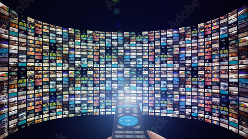 Image of big screen with many multi-colored channels, hands of man with remote control. photo