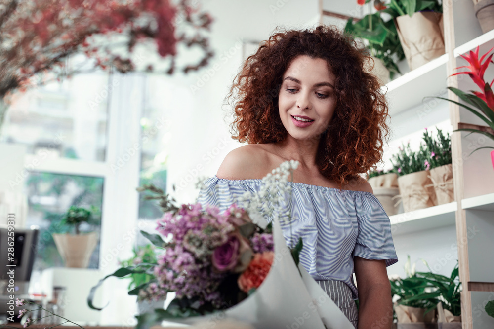 Satisfied good-looking curly-haired girl holding wrapped flowers