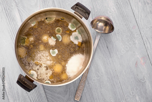 Moldy soup in a pot, poor storage concept, top view on wooden background with copy space.